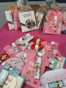 Assorted nurse-themed care packages and pink gift tags spread on a bright pink table, featuring small white vials and decorative bags in the background.