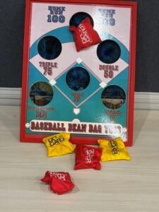 Bean bag toss game board with a baseball diamond layout and red and yellow bags on the floor in front of it.